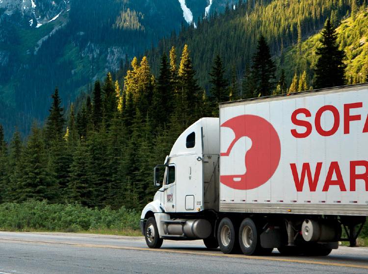 Truck with a visible brand logo on a road with mountains and trees in the background